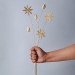 A hand holding a set of six Golden Spice Metal Sticks, featuring delicate star anise and cardamom-inspired designs with a gold finish against a neutral background.