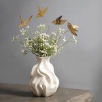 A wider view of the golden origami bird metal sticks displayed in a white artistic vase, styled with delicate white flowers for a chic home accent.