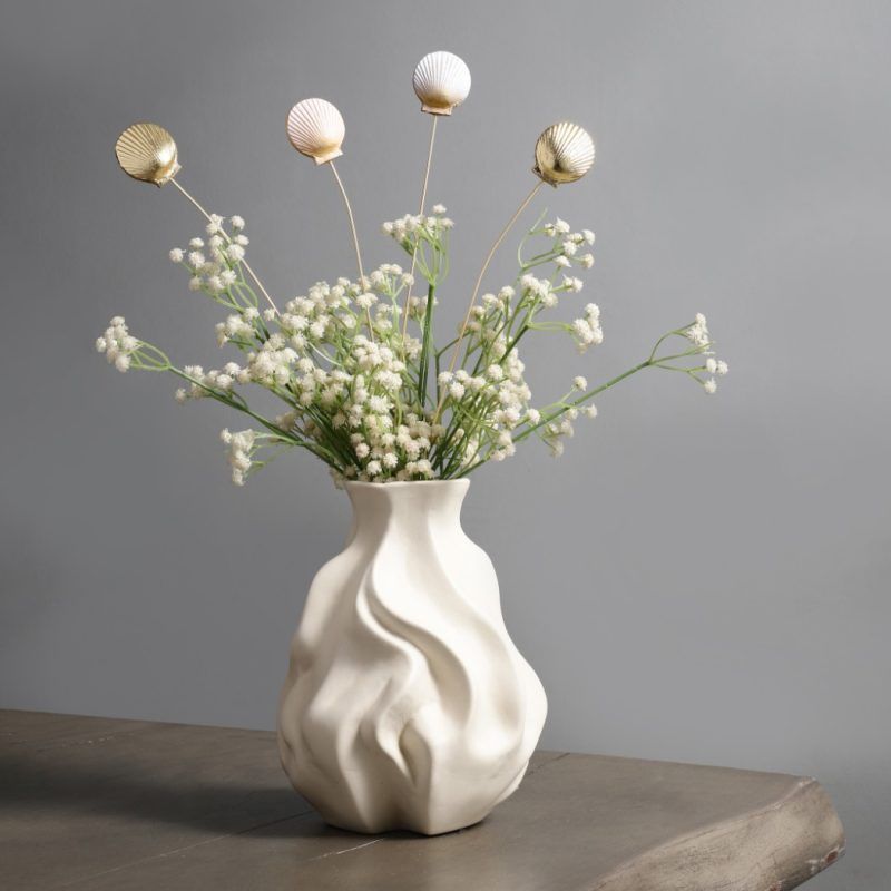 A set of 4 golden and golden-white seashell metal sticks arranged in a sculptural white vase, styled with delicate white florals for a coastal-inspired look.