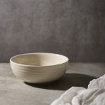 A glossy white ceramic bowl placed on a textured surface, with soft lighting highlighting its smooth finish.