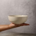 A hand holding a white ceramic bowl, illustrating its size and lightweight design.