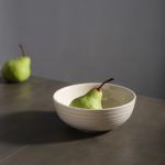 A white ceramic bowl with a fresh green pear inside, set on a sleek dark tabletop for a modern aesthetic.