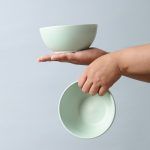 Two matte sage green ceramic thukpa bowls being held in separate hands, showcasing their size and lightweight design.