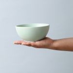 A single matte sage green ceramic bowl resting on an open palm, highlighting its smooth, minimalist design.