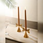 Golden Bow Candle Holders with warm-toned taper candles, set on a minimal linen table runner. Their sophisticated gold finish and bow-inspired silhouette add an elegant touch to any décor.