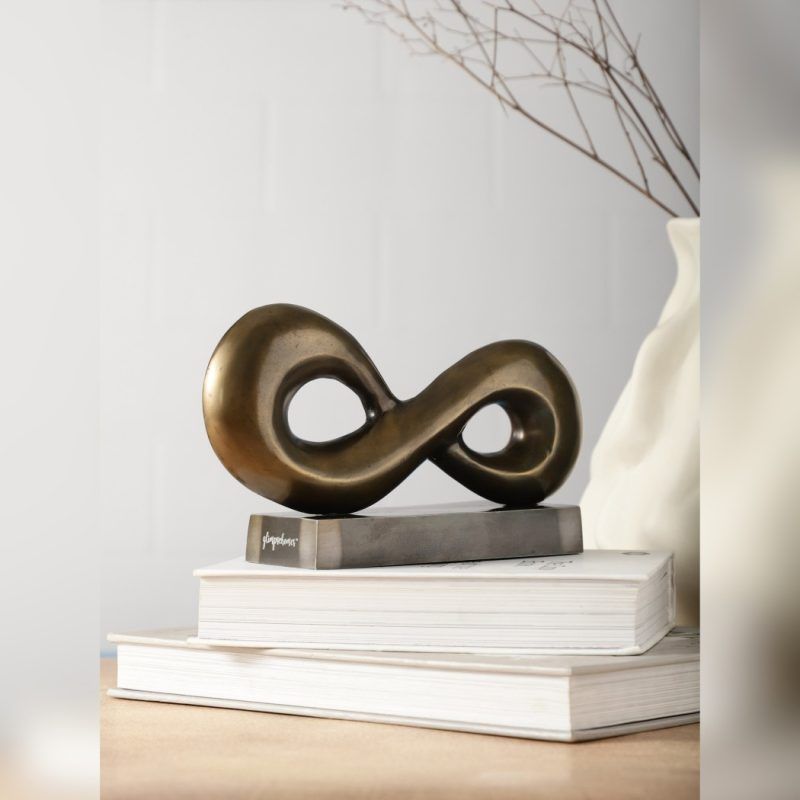 Side view of the aluminium infinity loop sculpture showing the depth and curvature, with the metal base detached and visible separately.