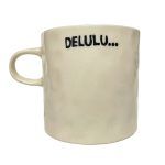 white background image of an off-white, textured ceramic mug. The mug has the word “DELULU…” printed in bold black letters.