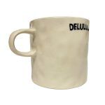 white background image of an off-white, textured ceramic mug. The mug has the word “DELULU…” printed in bold black letters.