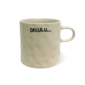 A beige ceramic mug with a slightly textured surface and a handle, featuring the text "DELULU..." written in black capital letters with three dots, set against a white background.