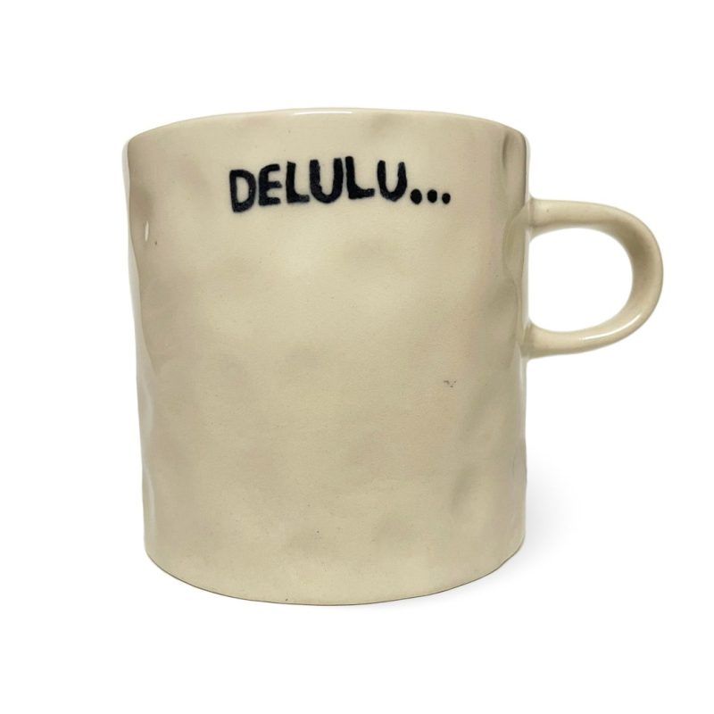 white background image of an off-white, textured ceramic mug. The mug has the word “DELULU…” printed in bold black letters.