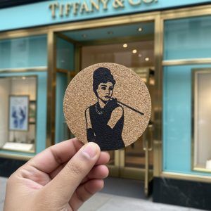 Cork coaster featuring Audrey Hepburn design held in hand outside Tiffany & Co. store.