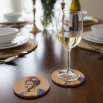 2 cork coasters featuring Frida Kahlo design, with a glass of white wine placed on top of one of the coasters on a dining table.