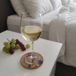 Cork coaster featuring Frida Kahlo design with a glass of white wine placed on top, on a bedside table with grapes.