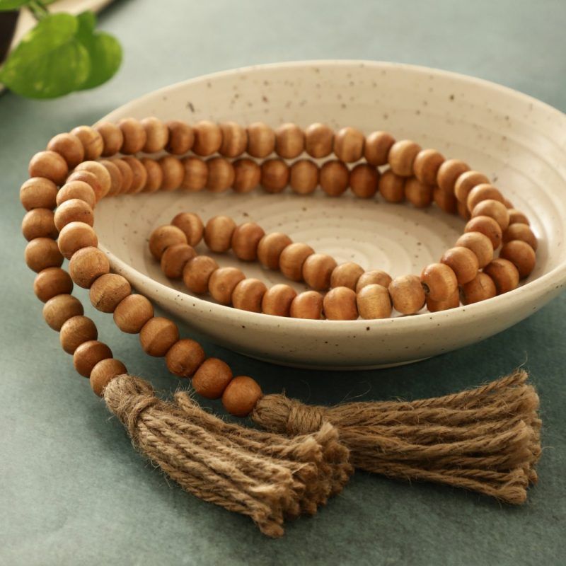 Farmhouse wooden bead garland in natural finish with jute tassels in ceramic bowl.