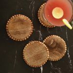 4 round wooden bead coasters in natural finish on black marble tabletop with drink glass.