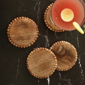 4 round wooden bead coasters in natural finish on black marble tabletop with drink glass.