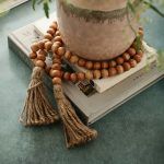 Rustic wooden bead garland in natural finish with tassels styled on coffee table books and vase.