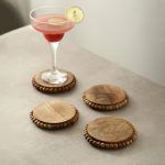 Set of 4 round wooden bead coasters in natural finish used with cocktail glass on table.