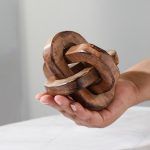 A hand holding a small Triple Knot Wooden Accent Piece, handmade natural decor.
