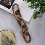 Decorative wooden chain link sculpture on a marble table next to an open book and potted plant.