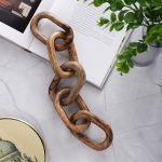 Decorative wooden chain link sculpture on a marble table next to an open book and potted plant.