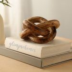 Wooden three-knot decor sculpture in brown tones atop stacked books on a table.