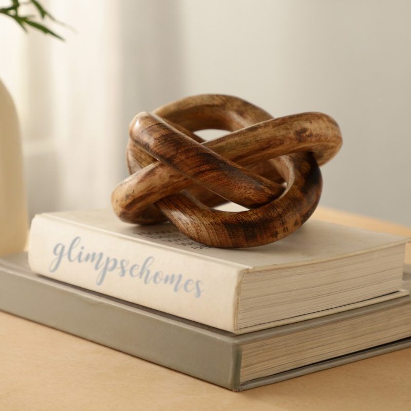 Wooden three-knot decor sculpture in brown tones atop stacked books on a table.