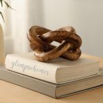 Wooden three-knot decor sculpture in brown tones atop stacked books on a table.