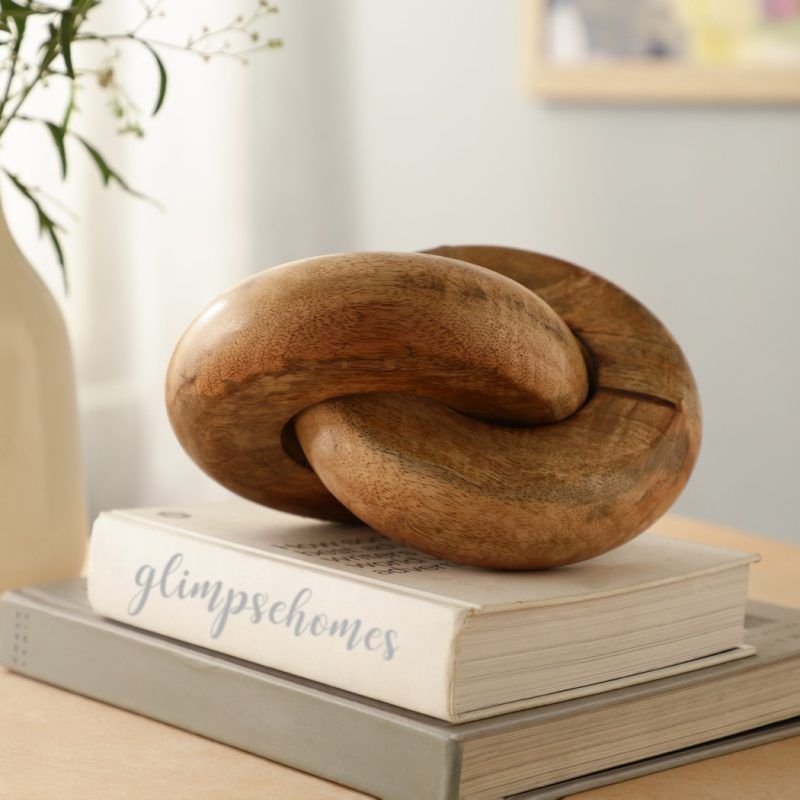 Wooden chain link decor with two knots in natural finish styled on books for home display.