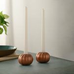 Set of two rose gold pumpkin candle holders with white taper candles on table.