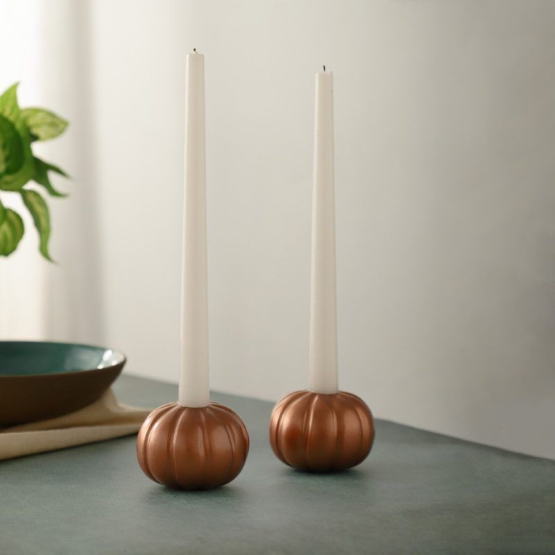 Set of two rose gold pumpkin candle holders with white taper candles on table.