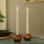 Rose gold pumpkin taper candle holders with burning candles on modern table.