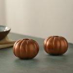 Pair of metallic rose gold pumpkin candle holders for taper candles on tabletop.