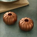 Top view of rose gold pumpkin-shaped taper candle holders on textured green surface.