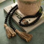 Black farmhouse wooden bead garland with jute tassels styled on books and vase.