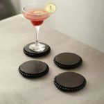 4 round wooden bead coasters in black finish styled with cocktail glass on table.