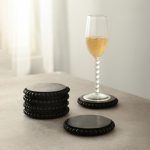 6 stacked round wooden bead coasters in black finish with champagne glass on table.