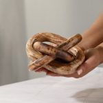 Hand holding a carved wooden three-knot decor piece with natural brown finish.