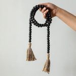 a hand holding a handcrafted black wooden bead garland with jute tassels, rustic farmhouse decor.