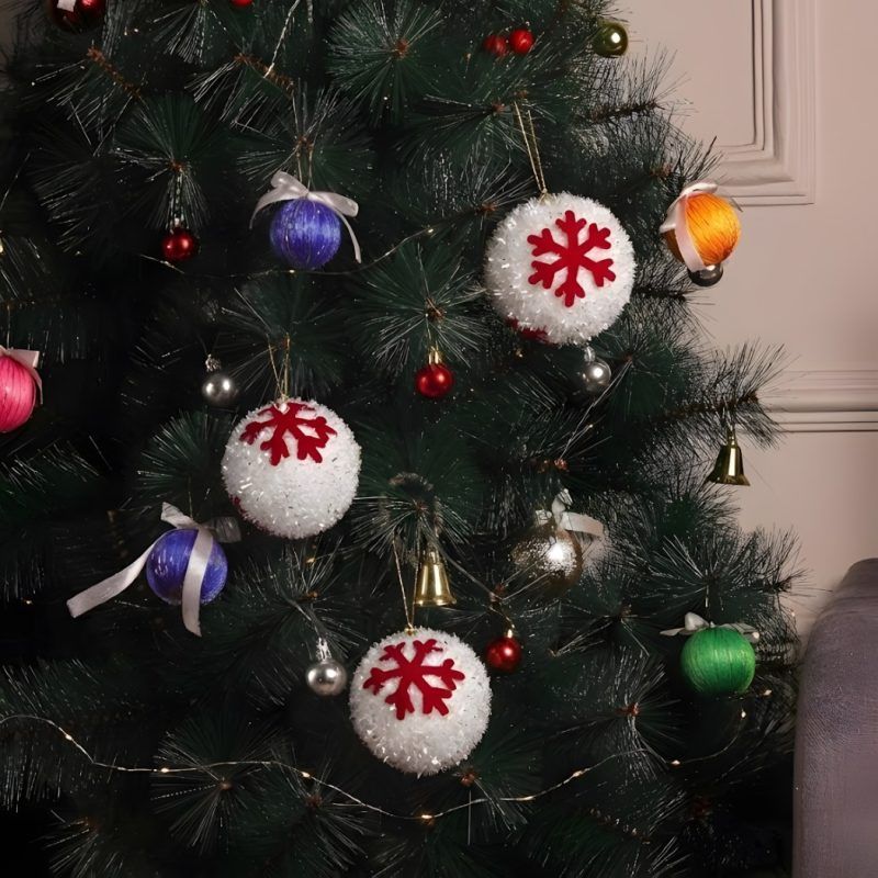 christmas-tree-decorated-with-3-white-snowball-ornaments A fully decorated Christmas tree featuring three white frosted snowball ornaments hanging alongside colorful wrapped baubles and bells.