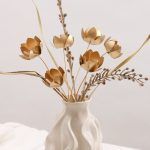 Detail shot of a set of 6 golden lotus metal flowers styled with dry grass in a vase, highlighting the volume of the bunch.