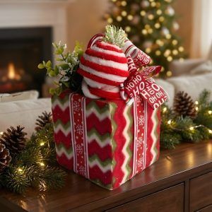 Close-up of a red and green chevron patterned Christmas gift box decor piece with a peppermint topper sitting on a wooden table.