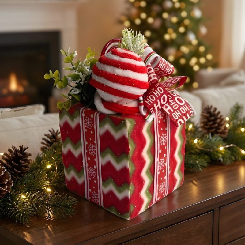decorative-christmas-box-chevron-pattern Close-up of a red and green chevron patterned Christmas gift box decor piece with a peppermint topper sitting on a wooden table.