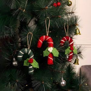 Three felt candy cane ornaments hanging on a green Christmas tree, showcasing a mix of red and green designs with felt holly leaf accents.