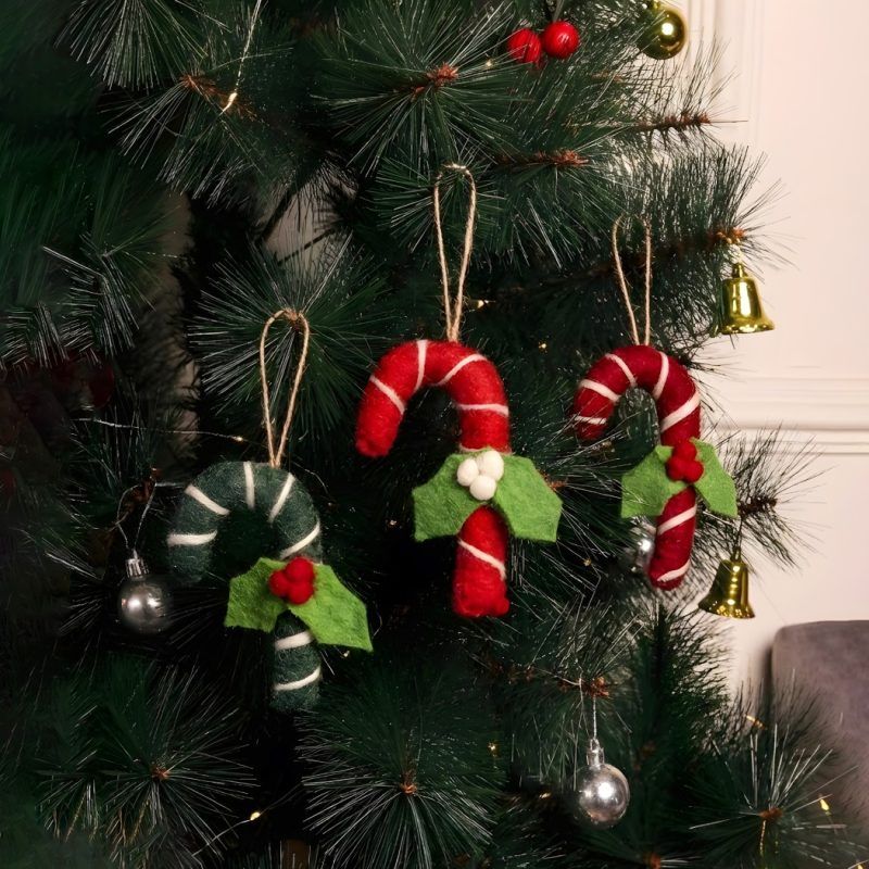 Three felt candy cane ornaments hanging on a green Christmas tree, showcasing a mix of red and green designs with felt holly leaf accents.