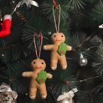 Two handmade felt gingerbread men ornaments hanging on a green Christmas tree.