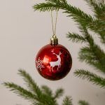 Glossy red Christmas ornament hanging on tree with white reindeer and snowflake silhouette design.