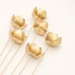 Six golden lotus metal sticks lying on a white surface, displaying the stem length and flower head shape for vase styling.