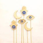 Top-down view of the Golden Persian Charm set of 6, displaying the detailed gold texture and blue accents of the Moon, Eye, and Hamsa symbols.