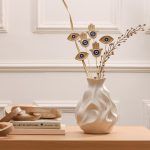 Full view of 6 golden Nazar vase filler sticks (3 Hamsa, 3 Evil Eye) mixed with dried flowers in a white vase on a wooden table.